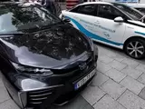 Zwei Toyota Mirai Wasserstoff-Brennstoffzellenfahrzeuge. Eines in schwarz, das andere in weiß mit geöffneter Motorhaube,